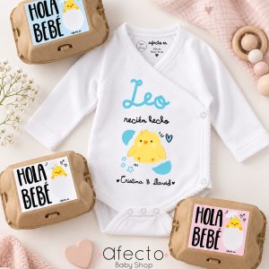 Body blanco de manga larga personalizado con el nombre del Bebé y un pollito, junto a tres hueveras kraft con etiquetas «Hola bebé».