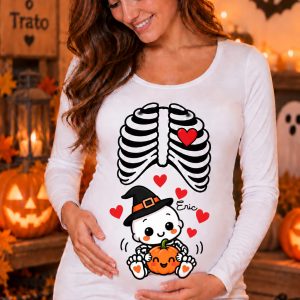 Modelo embarazada con camiseta blanca de manga larga y diseño de bebé esqueleto con gorro de bruja, calabaza kawaii y corazones rojos.